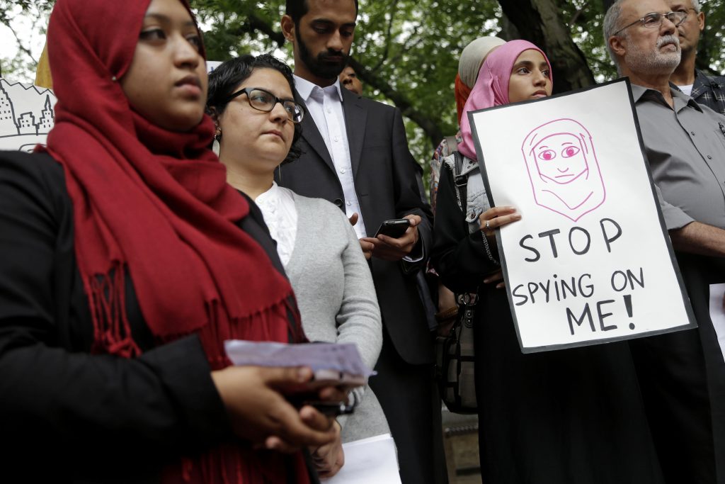 Muslim protesters gather, with one holding a sign that reads, "Stop spying on me."